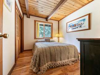 Experience cozy cabin living in this charming bedroom featuring a comfortable bed adorned with a textured throw and decorative pillows.