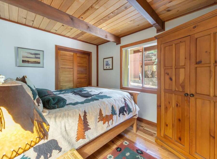 Experience rustic charm in this cozy bedroom, featuring a wooden beamed ceiling and a nature-themed comforter.
