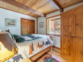 Experience rustic charm in this cozy bedroom, featuring a wooden beamed ceiling and a nature-themed comforter.