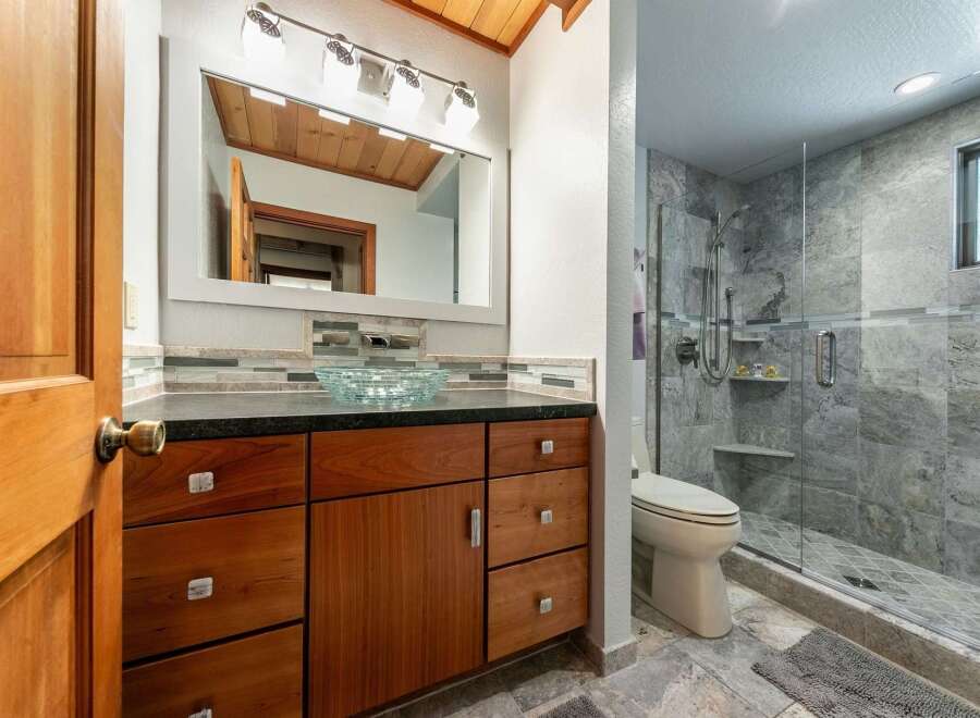 This modern bathroom features a sleek vanity with a glass vessel sink and ample storage, complemented by a spacious walk-in shower with elegant stone tilework.