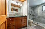 This modern bathroom features a sleek vanity with a glass vessel sink and ample storage, complemented by a spacious walk-in shower with elegant stone tilework.