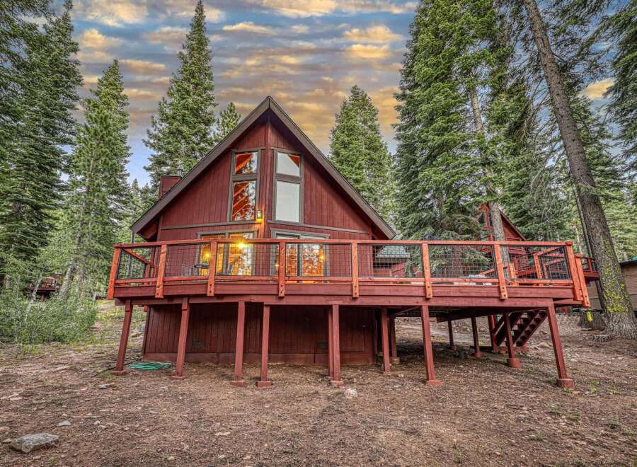 Experience the charm of this rustic red cabin nestled amongst tall evergreen trees.