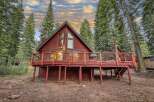 Experience the charm of this rustic red cabin nestled amongst tall evergreen trees.