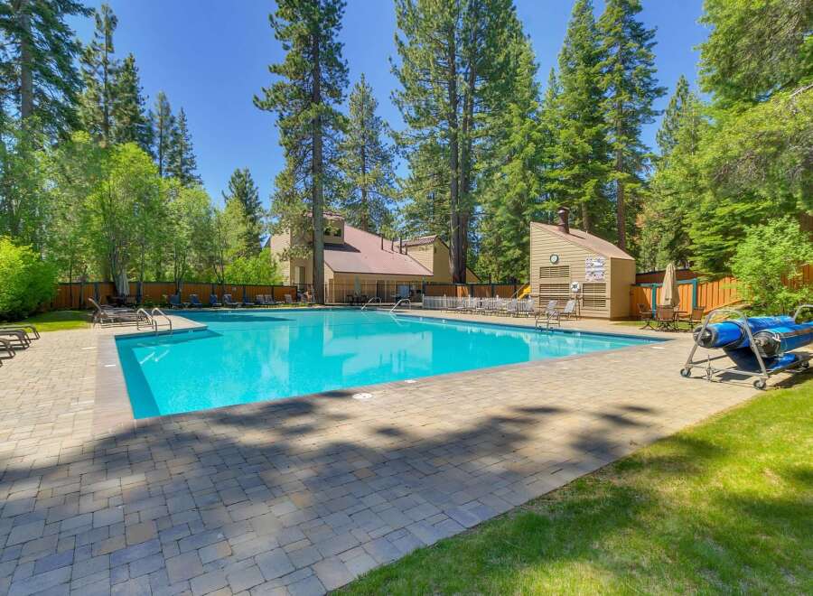 Enjoy a refreshing dip in the sparkling blue swimming pool, surrounded by lush green trees and a paved patio area.