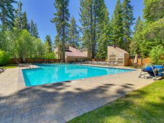 Enjoy a refreshing dip in the sparkling blue swimming pool, surrounded by lush green trees and a paved patio area.