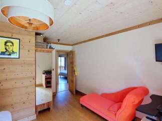 This charming room features a cozy ambiance with its warm wooden walls and ceiling, complemented by a striking orange chaise lounge.