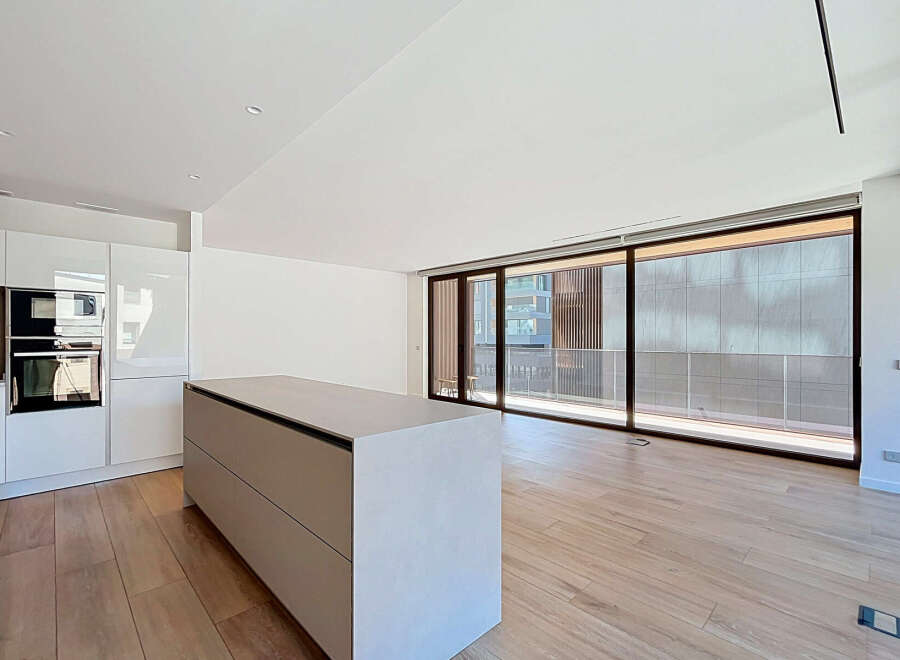 Experience modern living in this stunning open-plan kitchen and living area, featuring sleek white cabinetry and integrated appliances.