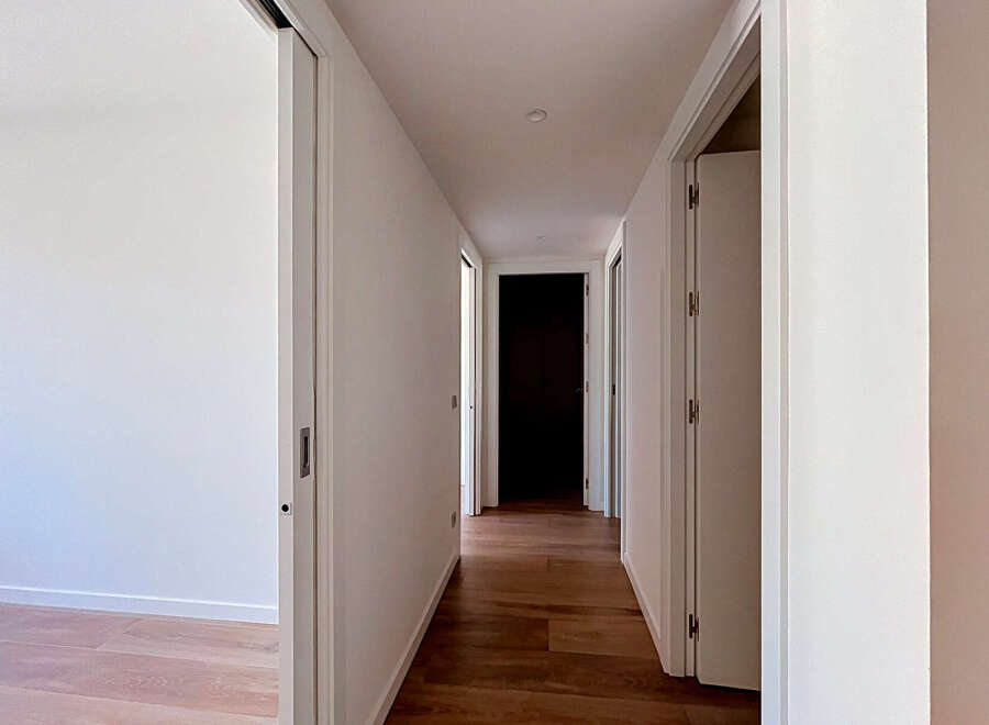 Step into this bright and airy hallway, featuring a sleek sliding door on the left and a passage leading to multiple rooms.
