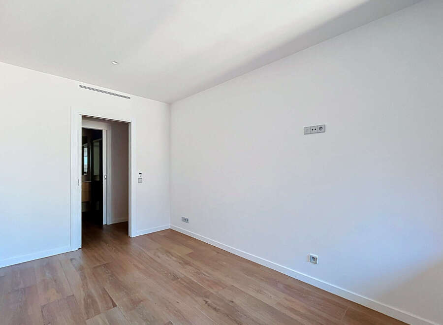 This spacious room features a clean, modern aesthetic with white walls and a sleek air vent.