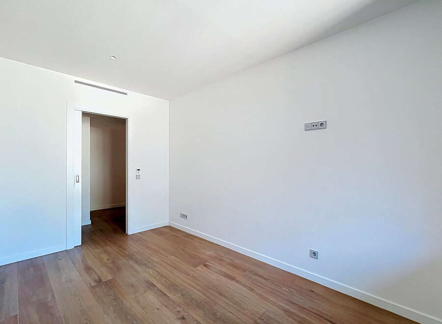 This spacious room features a clean, modern aesthetic with white walls and a sleek air vent.