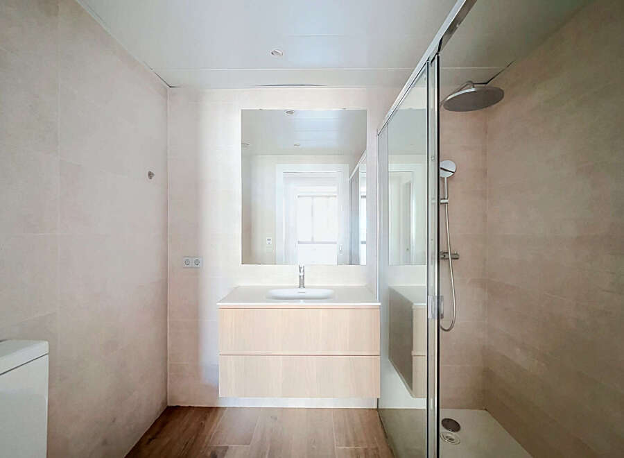 This modern bathroom features a sleek vanity with ample storage, a spacious walk-in shower with a rainfall showerhead, and a large vanity mirror.