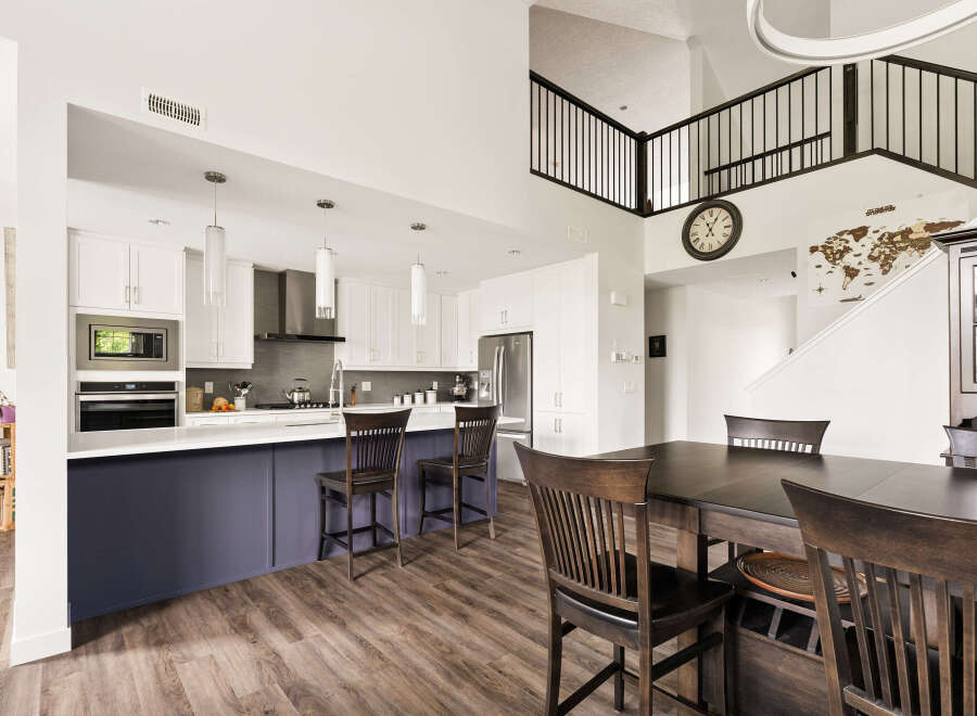 This spacious open-concept kitchen and dining area features a large island with seating, modern white cabinetry, and a sleek stainless steel range hood.