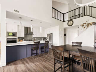 This spacious open-concept kitchen and dining area features a large island with seating, modern white cabinetry, and a sleek stainless steel range hood.