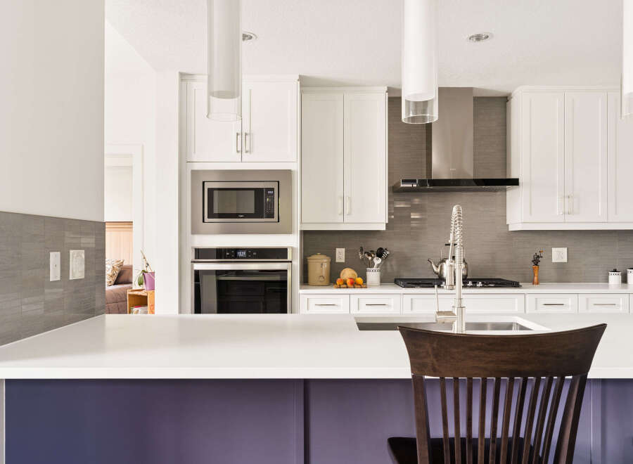 Experience modern luxury in this stunning kitchen, featuring sleek white cabinetry, a stainless steel range hood, and a sophisticated grey tile backsplash.
