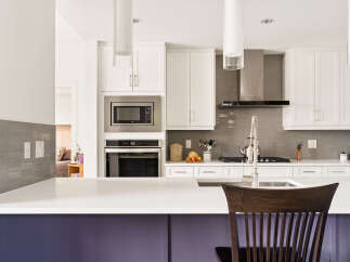 Experience modern luxury in this stunning kitchen, featuring sleek white cabinetry, a stainless steel range hood, and a sophisticated grey tile backsplash.