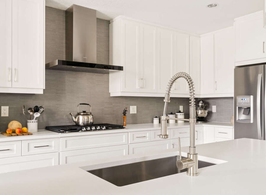 Experience modern kitchen luxury with sleek white cabinetry, a sophisticated grey tiled backsplash, and a professional-grade stainless steel range hood.