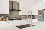 Experience modern kitchen luxury with sleek white cabinetry, a sophisticated grey tiled backsplash, and a professional-grade stainless steel range hood.