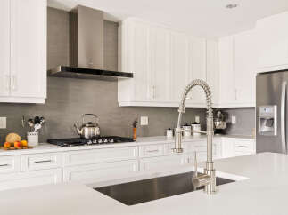 Experience modern kitchen luxury with sleek white cabinetry, a sophisticated grey tiled backsplash, and a professional-grade stainless steel range hood.