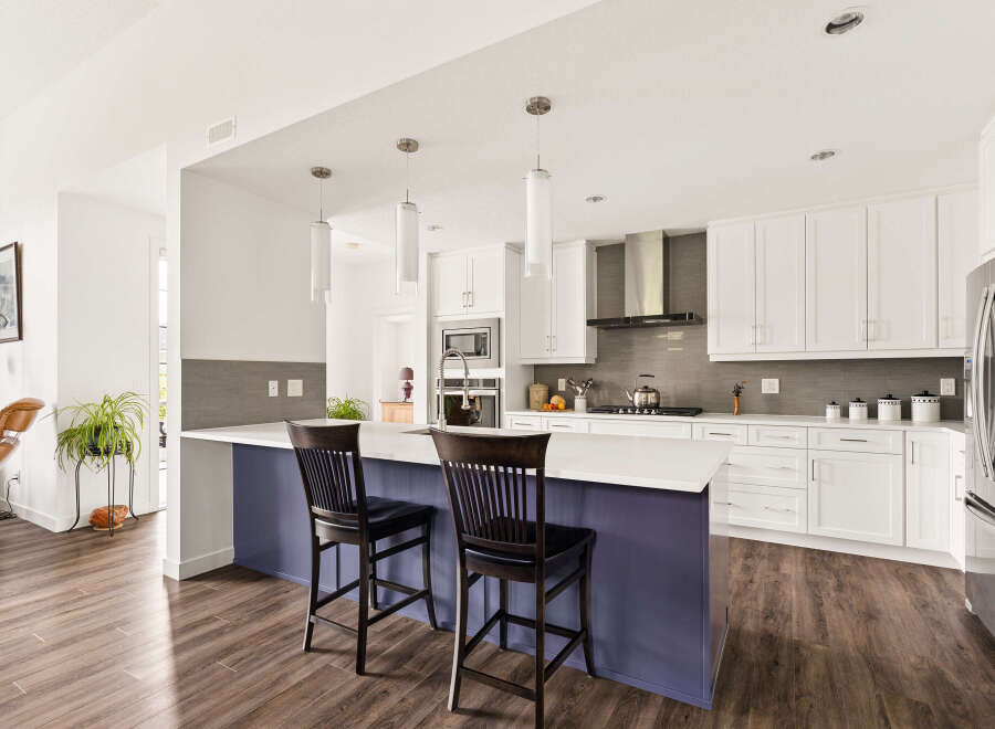 Experience modern living in this stunning kitchen featuring sleek white cabinetry, a spacious island with a purple base, and a sophisticated grey tiled backsplash.