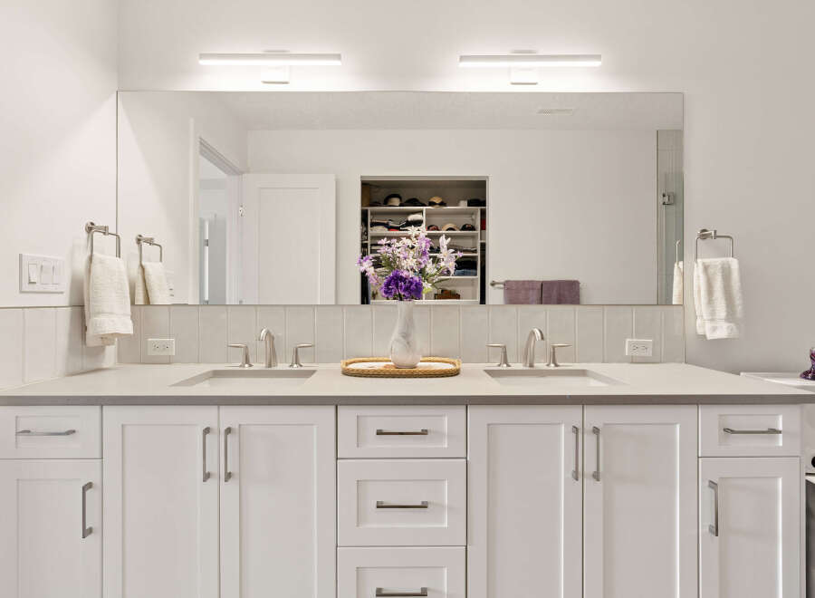 This modern bathroom features a spacious double vanity with two sinks, sleek brushed nickel faucets, and ample storage beneath.