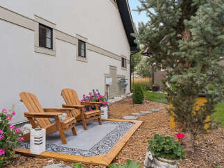 Enjoy outdoor living with this charming patio featuring two Adirondack chairs and a decorative rug, perfect for relaxing evenings.