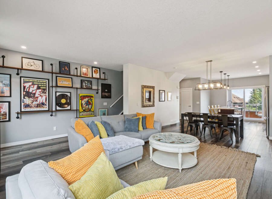 This open-concept living and dining area boasts a stylish grey sectional sofa adorned with vibrant yellow and blue throw pillows, complemented by a unique coffee table with a glass top and intricate detailing.