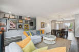 This open-concept living and dining area boasts a stylish grey sectional sofa adorned with vibrant yellow and blue throw pillows, complemented by a unique coffee table with a glass top and intricate detailing.