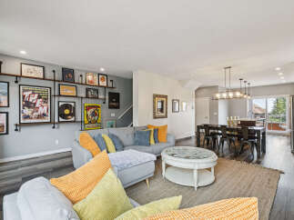 This open-concept living and dining area boasts a stylish grey sectional sofa adorned with vibrant yellow and blue throw pillows, complemented by a unique coffee table with a glass top and intricate detailing.