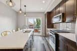 This modern kitchen boasts dark wood cabinetry, a sleek quartz countertop island with a double sink, and stainless steel appliances including a microwave and gas range.