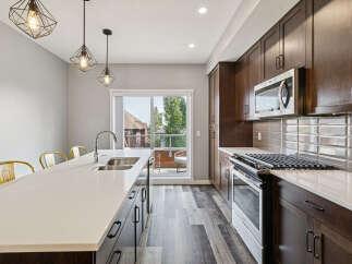 This modern kitchen boasts dark wood cabinetry, a sleek quartz countertop island with a double sink, and stainless steel appliances including a microwave and gas range.