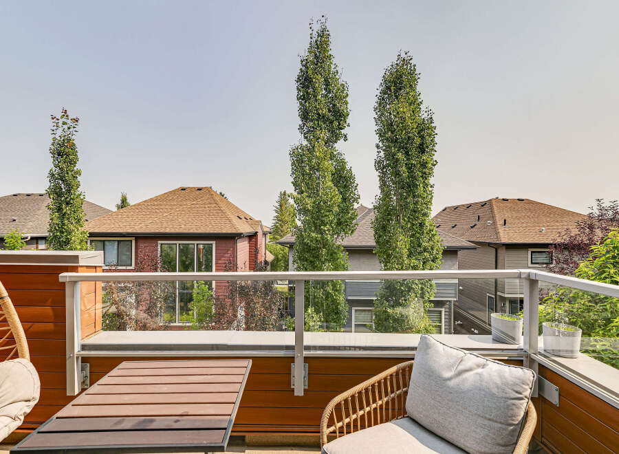 Enjoy outdoor living on this modern balcony, featuring a comfortable seating area with a hanging chair and a stylish wicker chair with cushions.