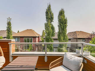 Enjoy outdoor living on this modern balcony, featuring a comfortable seating area with a hanging chair and a stylish wicker chair with cushions.