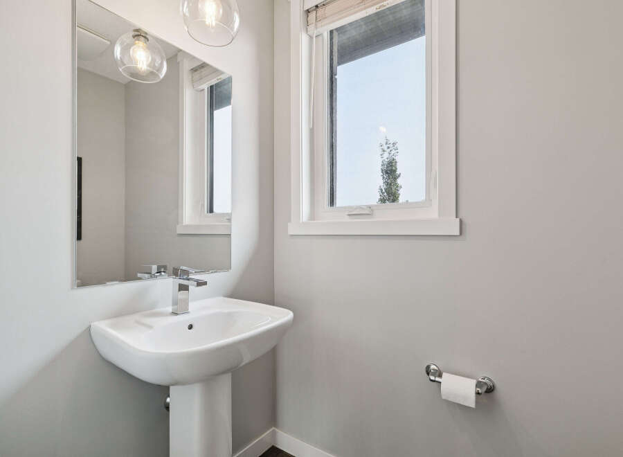 This modern bathroom features a sleek pedestal sink with a chrome faucet, complemented by a large vanity mirror and elegant pendant lighting.