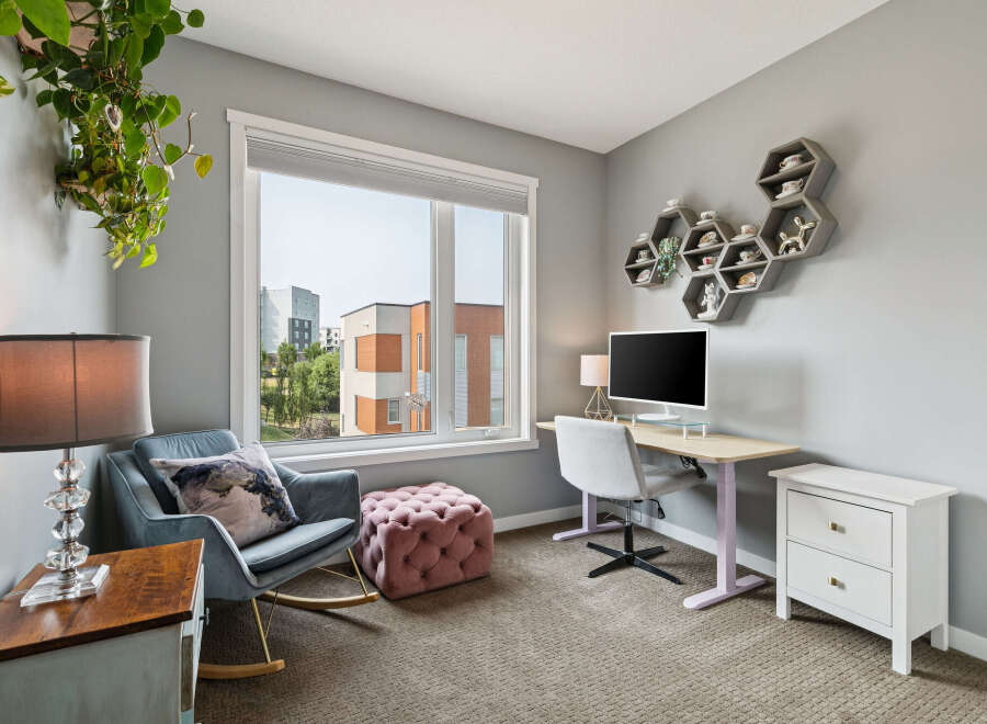 This home office features a comfortable rocking chair with a decorative pillow, a plush ottoman, and a stylish desk with a computer.