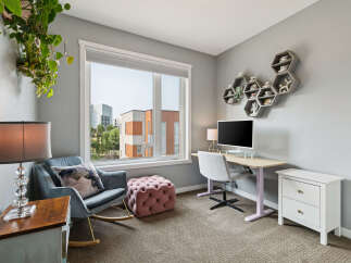This home office features a comfortable rocking chair with a decorative pillow, a plush ottoman, and a stylish desk with a computer.
