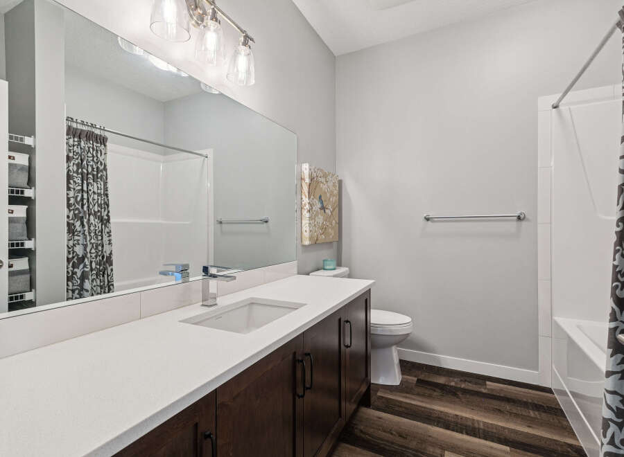 This modern bathroom features a sleek vanity with a white quartz countertop and dark wood cabinetry, complemented by a large mirror and stylish light fixtures.