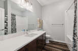 This modern bathroom features a sleek vanity with a white quartz countertop and dark wood cabinetry, complemented by a large mirror and stylish light fixtures.