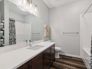This modern bathroom features a sleek vanity with a white quartz countertop and dark wood cabinetry, complemented by a large mirror and stylish light fixtures.