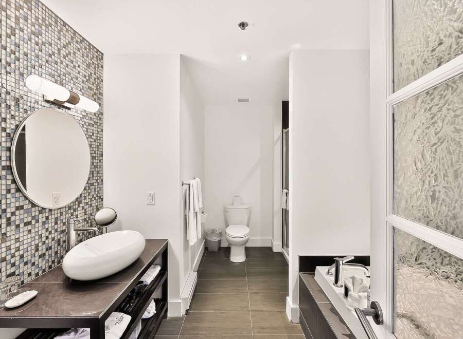 Experience modern luxury in this stunning bathroom featuring a sleek vessel sink atop a dark vanity, complemented by a striking mosaic tile accent wall.