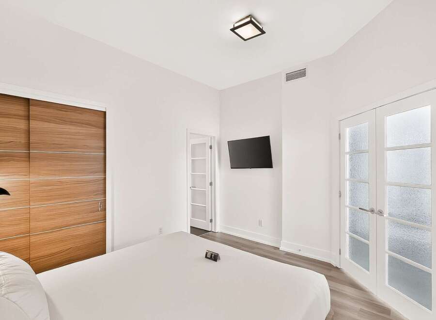 Experience modern luxury in this beautifully appointed bedroom, featuring a sleek wall-mounted TV and a stylish wood-paneled closet.