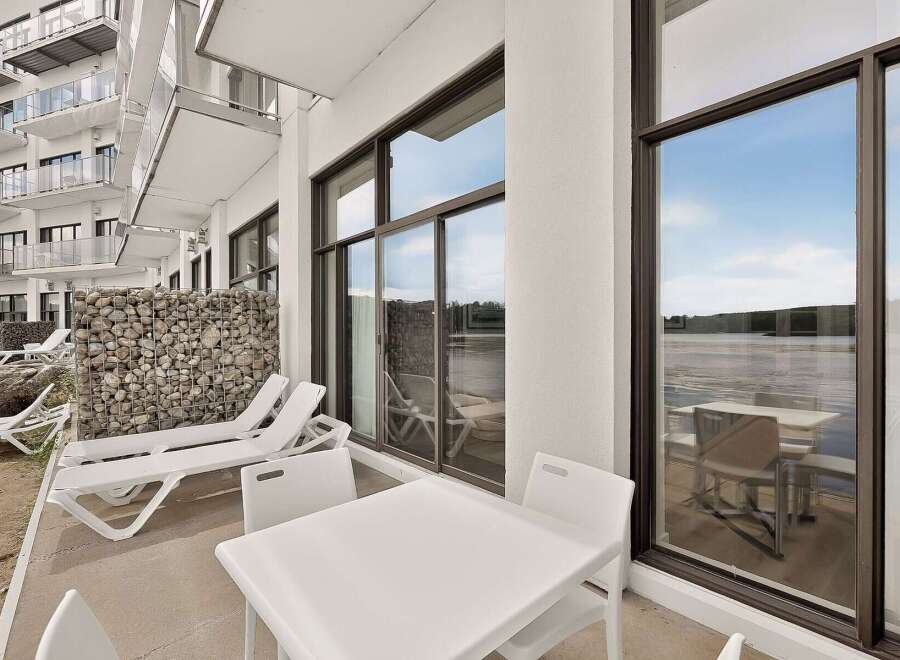 Enjoy stunning waterfront views from this modern property featuring a spacious balcony with comfortable lounge chairs and a dining set.