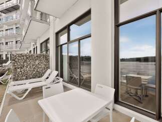 Enjoy stunning waterfront views from this modern property featuring a spacious balcony with comfortable lounge chairs and a dining set.