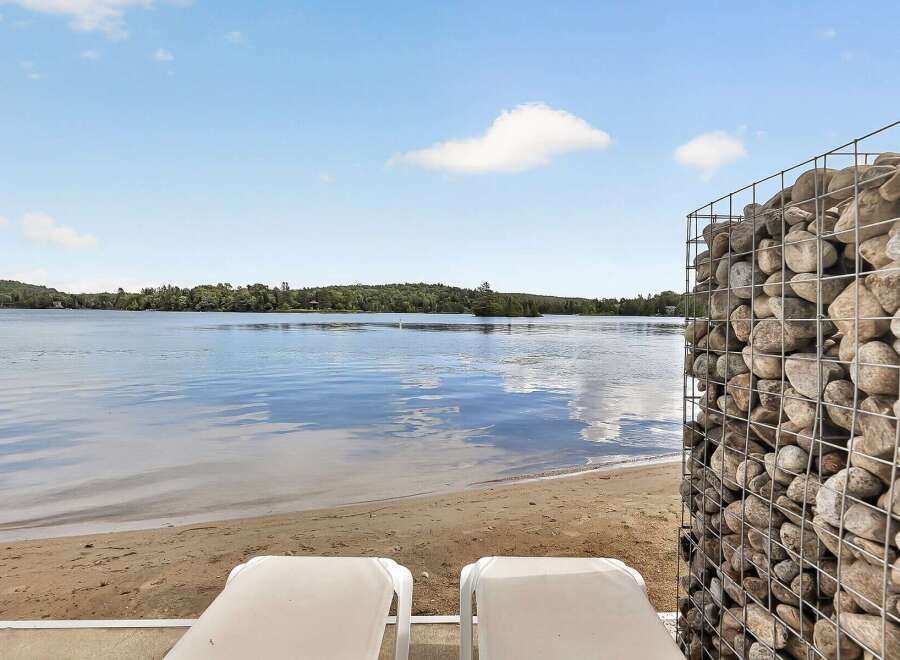 Enjoy serene lakefront living with this stunning property featuring a private sandy beach and two comfortable lounge chairs perfect for soaking up the sun.
