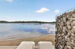 Enjoy serene lakefront living with this stunning property featuring a private sandy beach and two comfortable lounge chairs perfect for soaking up the sun.