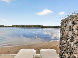 Enjoy serene lakefront living with this stunning property featuring a private sandy beach and two comfortable lounge chairs perfect for soaking up the sun.