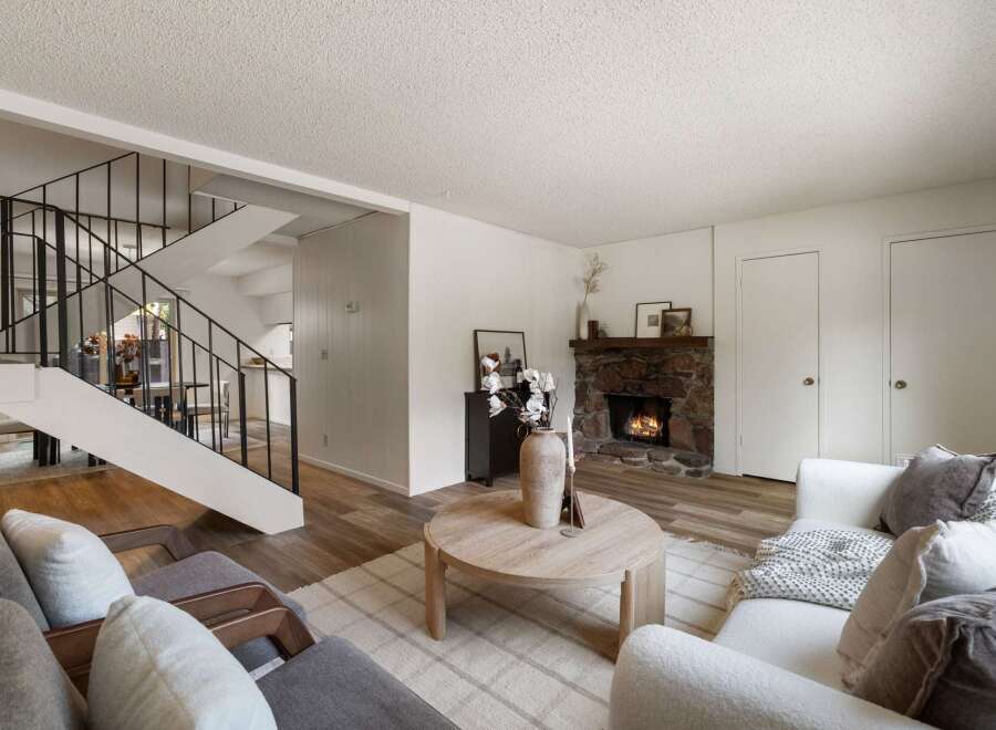 Cozy living room featuring a stone fireplace and a modern staircase.