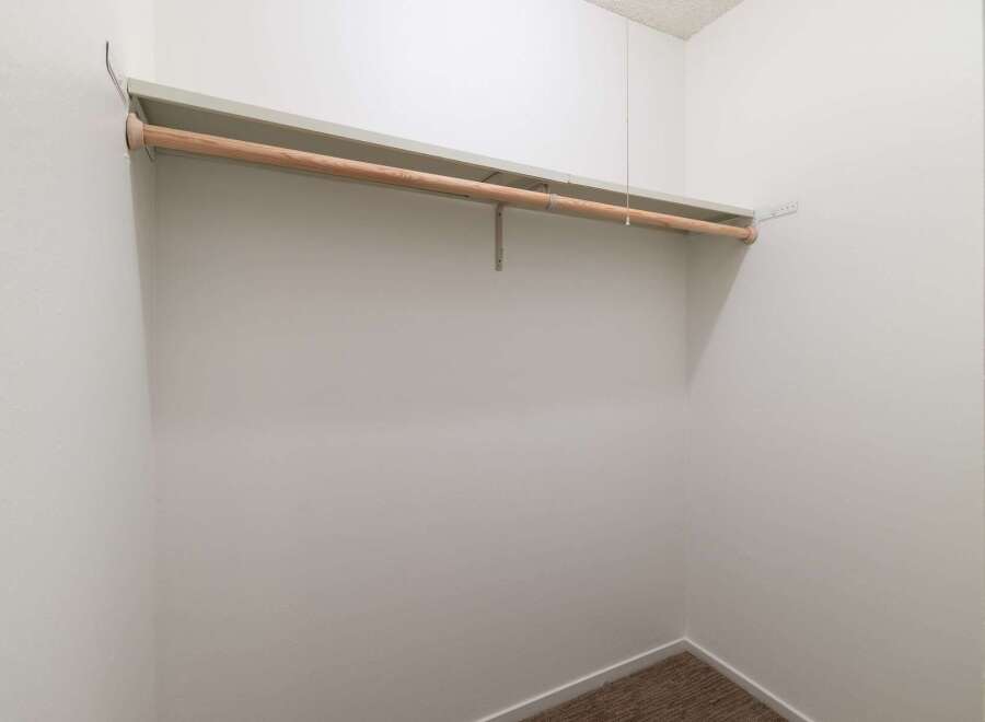 This spacious walk-in closet offers ample storage with a sturdy wooden rod and a built-in shelf, perfect for organizing your wardrobe.