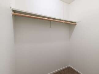 This spacious walk-in closet offers ample storage with a sturdy wooden rod and a built-in shelf, perfect for organizing your wardrobe.