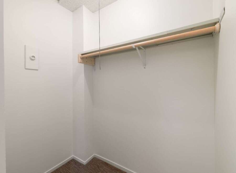 Discover ample storage in this spacious walk-in closet, featuring a sturdy wooden hanging rod and a convenient wall-mounted shelf.