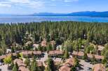Discover this stunning aerial view showcasing a charming residential community nestled amidst a dense forest, with a breathtaking lake and distant mountains forming a picturesque backdrop.